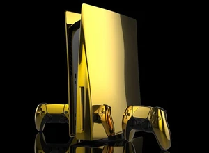 Золотая игровая консоль с двумя контроллерами на черном фоне.