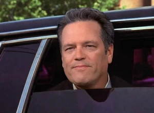 Мужчина с короткими волосами улыбается и выглядывает из окна лимузина.