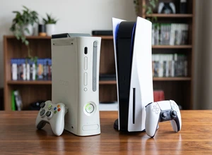 На столе стоят консоли Xbox 360 и PlayStation 5 рядом с геймпадами.