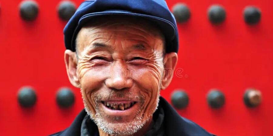 Улыбающийся пожилой мужчина на фоне красной стены с металлическими шипами.