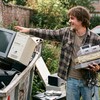 Парень в клетчатой рубашке показывает на мусорный контейнер с старыми компьютерами.