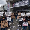 Толпа людей с плакатами на фоне здания GDC 2026. Обстановка протестная.