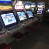 Ряд игровых автоматов с экранами и красными стульями в зале.