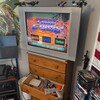 Старый телевизор на комоде с видеоигрой на экране, рядом игровые приставки и фильмы.