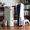 На столе стоят консоли Xbox 360 и PlayStation 5 рядом с геймпадами.